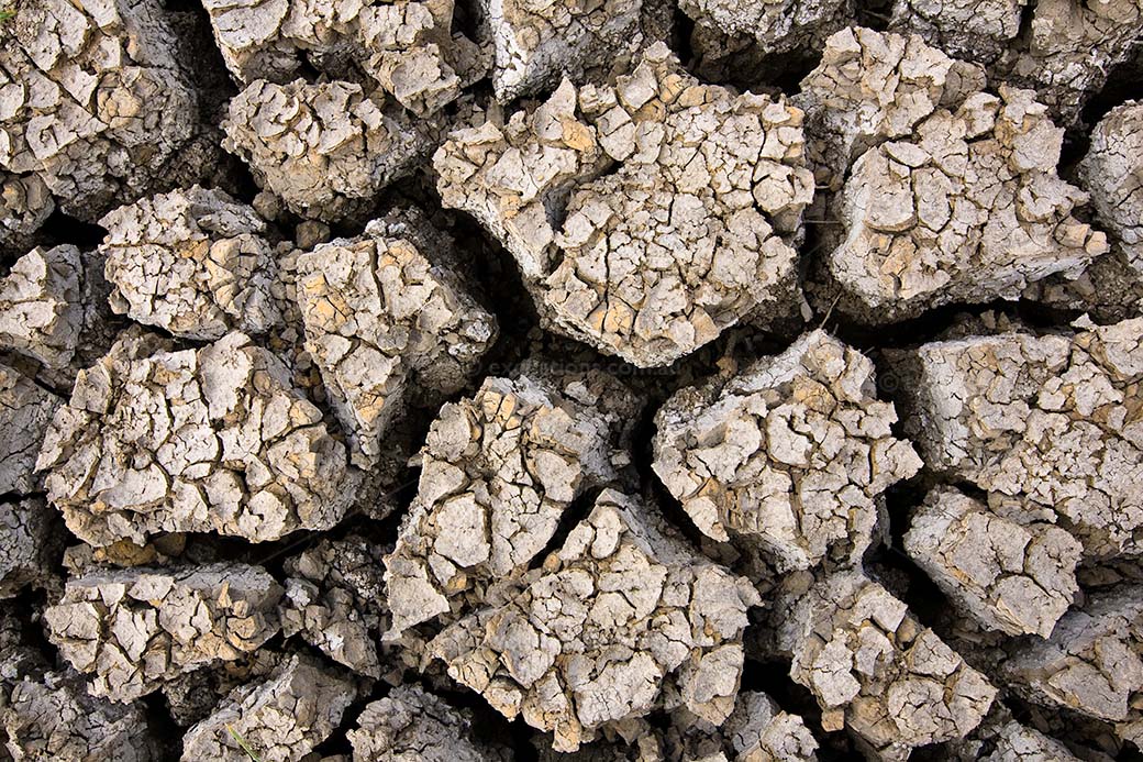 Deeply cracked drying mud, strong contrasts and very textured surface with smaller pieces of cracked mud on the surfaces of the large slabs