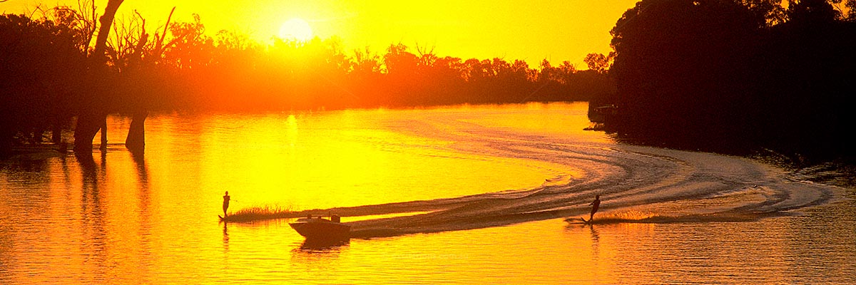 Dramatic photo of speed boat and water skiers on the Murray River near Mildura. Loverly golden tones. Stock photos of Mildura.