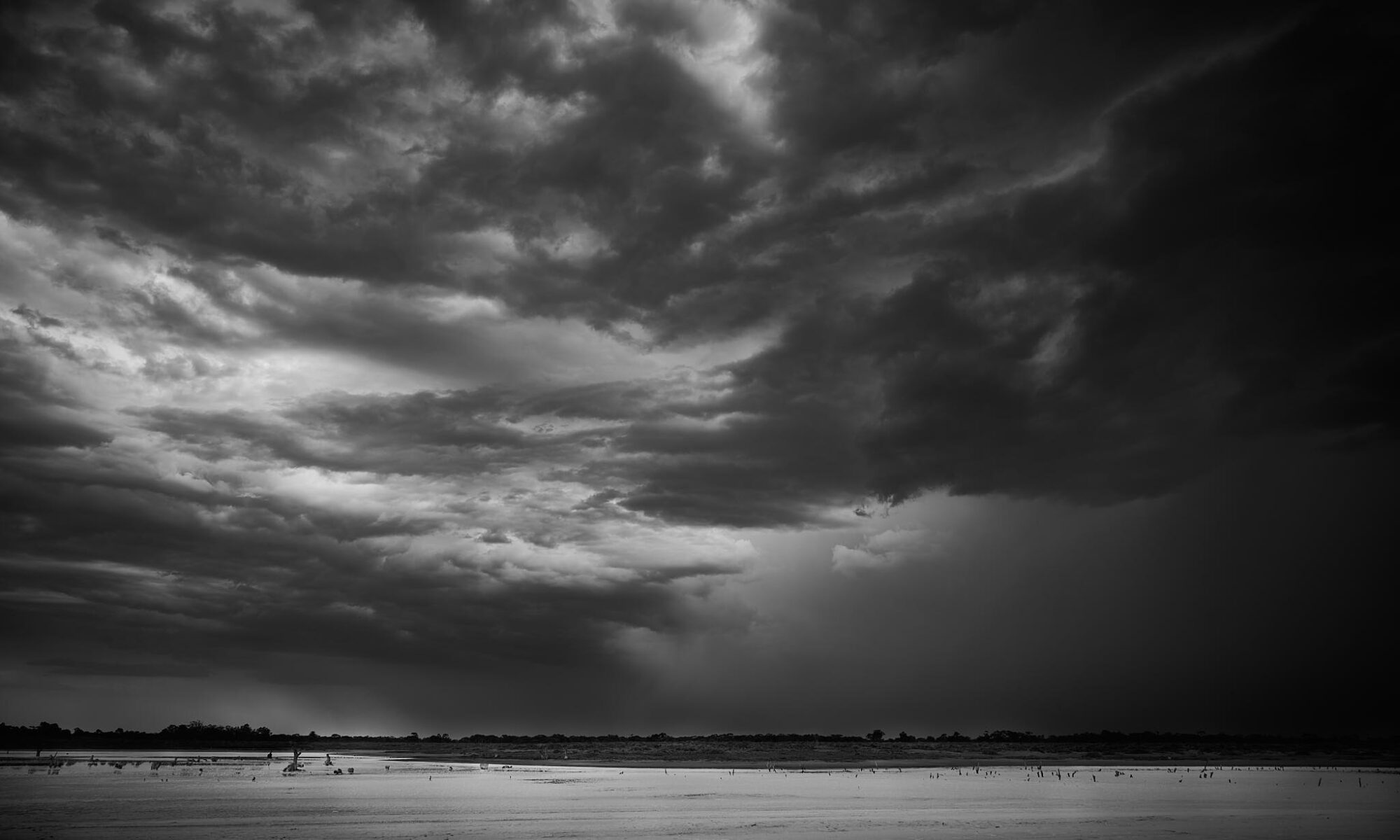 Monochrome photograph of storm clouds over an outback Australian salt lake.